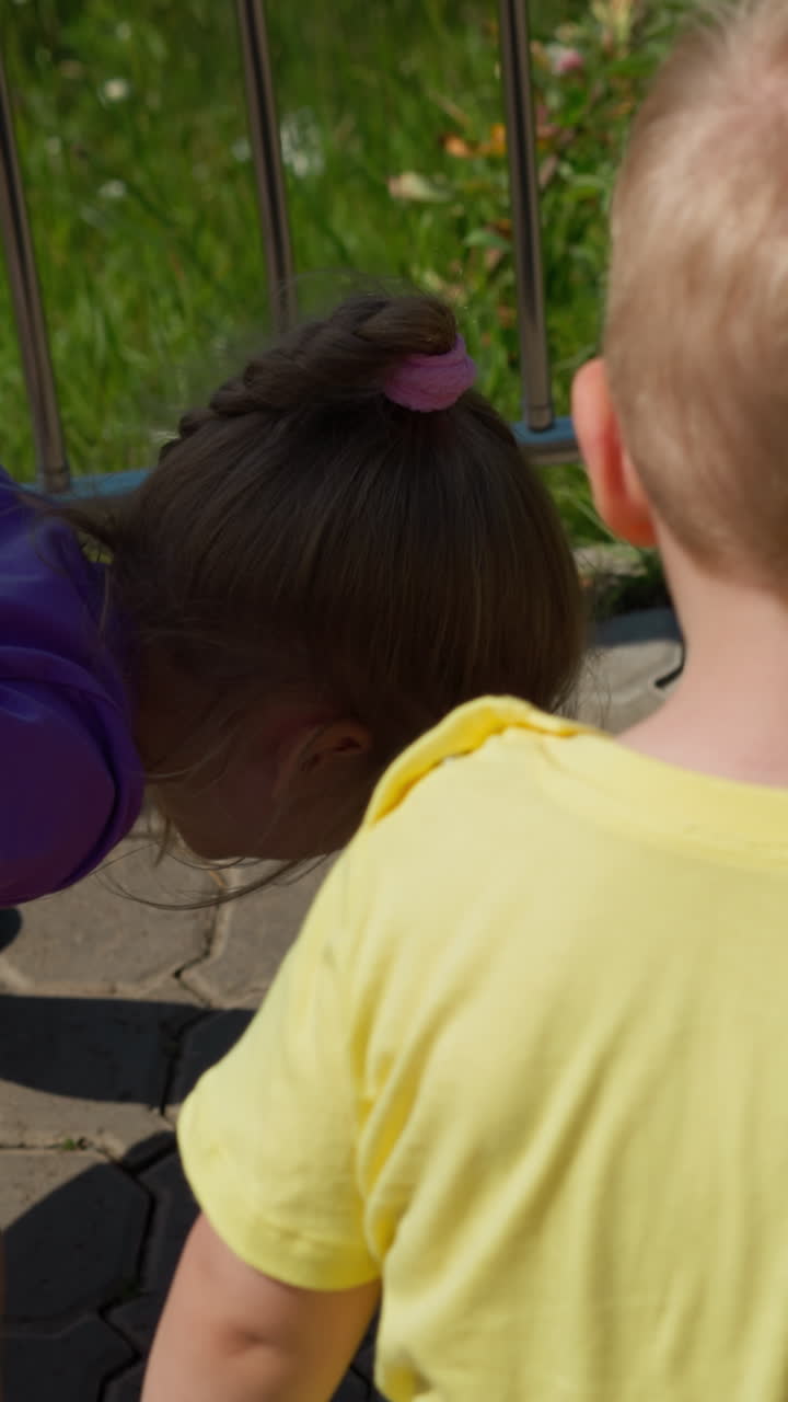 재미있는 어린 소녀는 달리는 개미를 두려워 멀리 뛰어, 은 날 푸른 공원에서 cobblestone 보행길에 동생 근처에 느린 동작을 뒷면 보기