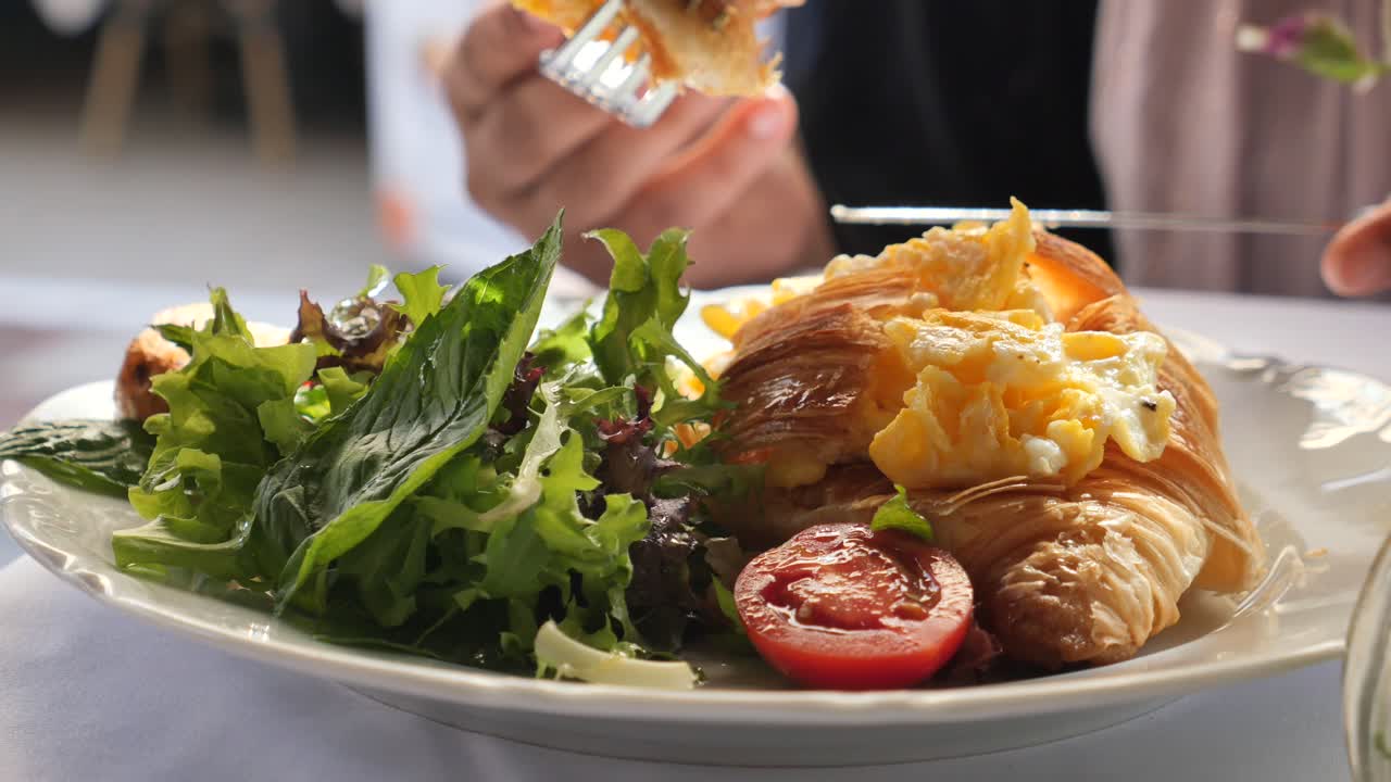 A croissant sandwich with salad and tomato being eaten