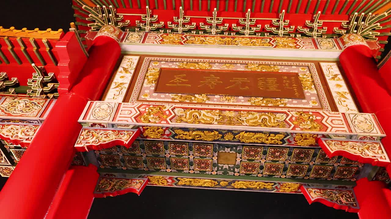 Camera tilts upward beneath illuminated Chinese gate, revealing intricate details and vibrant red pillars