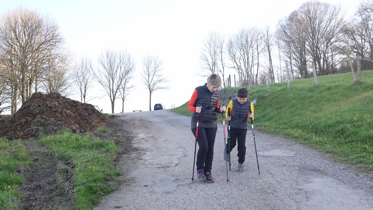 Mujer y niño haciendo marcha nórdica cuesta arriba por un camino rural