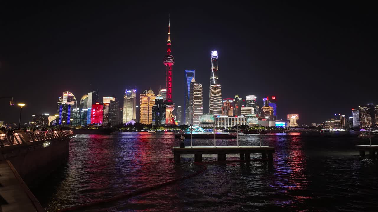 Time-lapse nocturno del emblemático skyline de Shanghái (Pudong) con la Torre Perla Oriental y la Torre de Shanghái reflejadas en la calma del río Huangpu, luces coloridas
