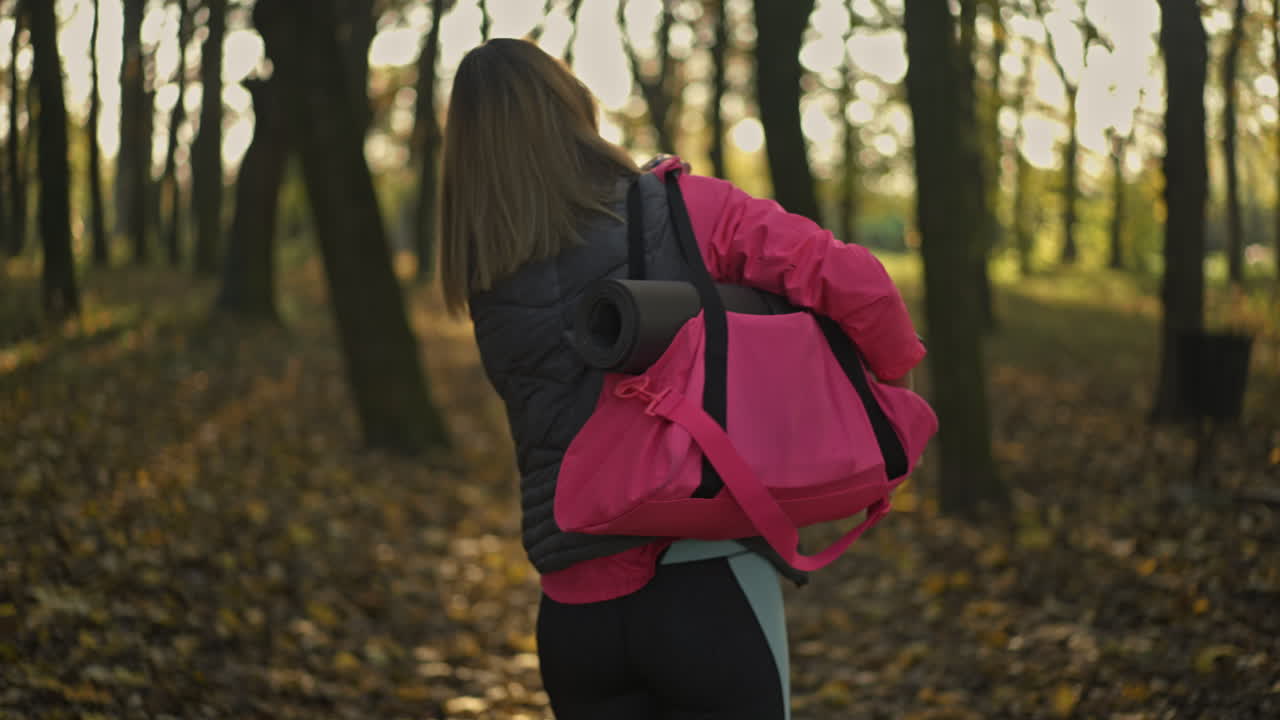 Woman walking through an autumn park with her gym bag and yoga mat
