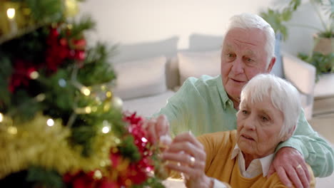 una feliz pareja caucásica decorando el árbol de navidad en casa, en cámara lenta.