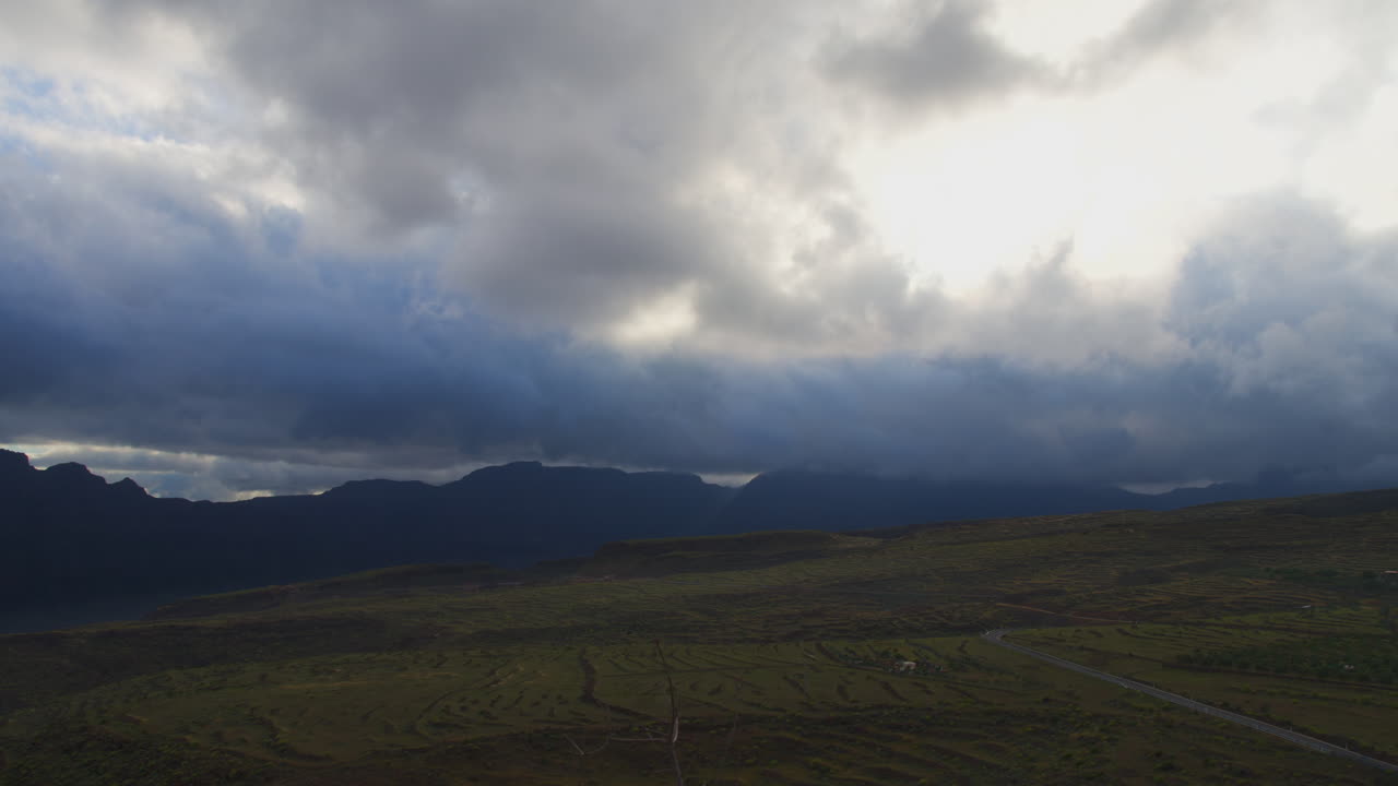 Dramatic cloudscape racing across rugged volcanic terrain of Gran canaria, revealing dynamic interplay of light, shadow, and expansive island scenery