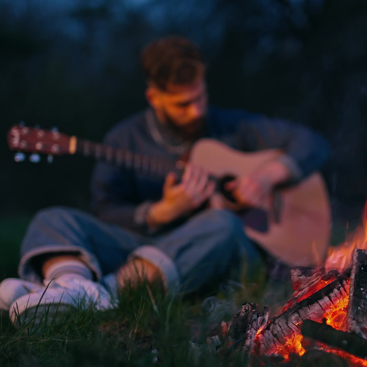 Man sits by fire playing the guitar. Man with guitar resting near bonfire outdoors at night