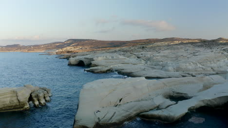 Toma-Aérea-De-Un-Dron-Circular-De-Una-Persona-En-La-Playa-De-Sarakiniko,-Paisaje-Lunar-En-La-Isla-De-Milos,-Grecia-Con-Luz-Dorada