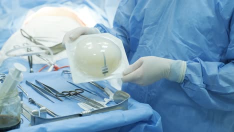 the surgeon prepares a sterile silicone breast implant for breast augmentation surgery