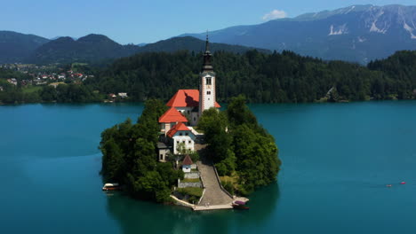 Vista-Aérea-De-La-Isla-De-Bled-Con-Cafetería,-Casa-Preboste-E-Iglesia-De-Peregrinación-De-La-Asunción-De-María-Junto-Al-Lago-En-Bled,-Eslovenia