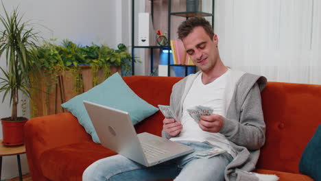 smiling happy man counting money cash and use laptop pc calculate domestic income earnings at home