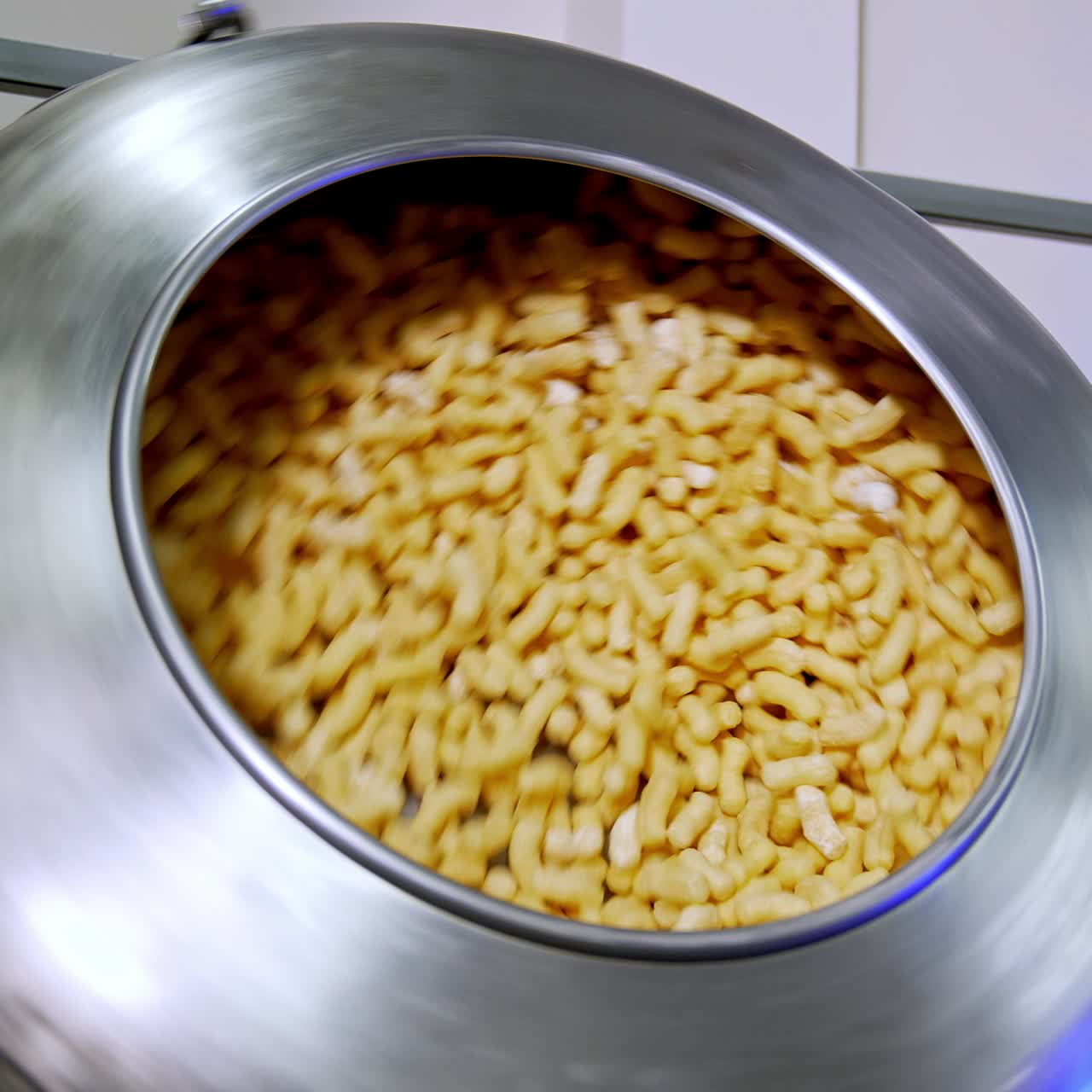 Metal tank rotating and mixing the corn snacks inside. Thick maize sticks are covered with sugar glazing. Food factory production