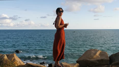 Woman-in-red-dress-standing-on-rocky-shore-with-ocean-backdrop-at-Con-Dao-island