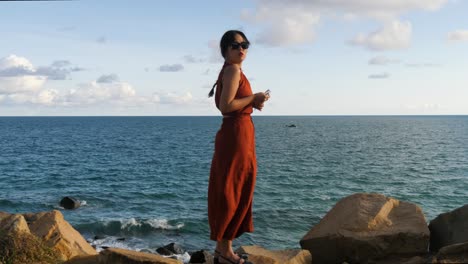 woman in red dress standing on rocky shore with ocean backdrop at con dao island