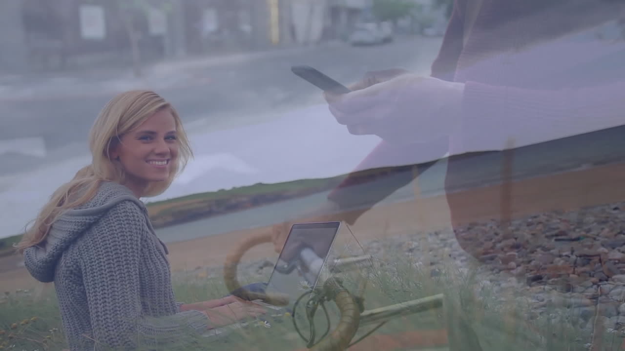 Using laptop outdoors, woman with animation overlay of person holding smartphone