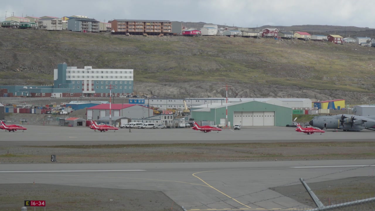 Mellemdistanceoptagelse der følger fem RAF Red Arrows BAE Hawk jetfly, mens de taxier i rækkefølge mod landingsbanen forbi et massivt RAF A400M Atlas militært transportfly
