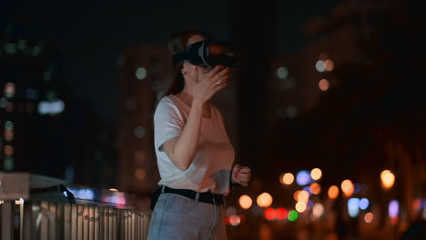 una joven con gafas de realidad virtual en la ciudad nocturna mueve sus manos dominando la interfaz de la aplicación. vr tecnologías del futuro en la vida cotidiana. juegos de realidad virtual