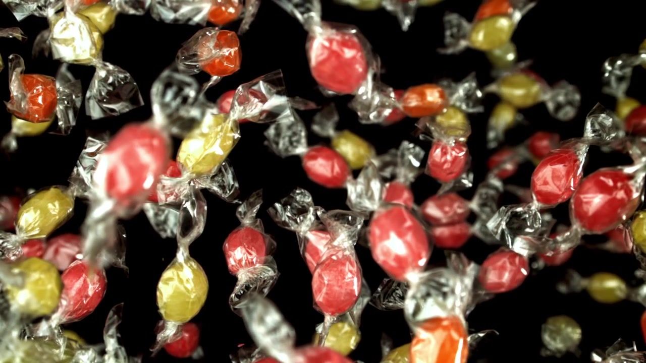 Caramelle colorate incartate che cadono al rallentatore su sfondo nero