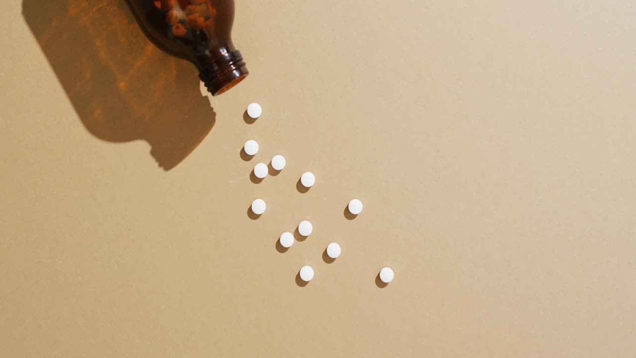 video de una botella marrón derramando píldoras blancas sobre un fondo marrón con espacio para copiar