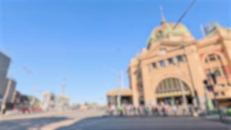 people crossing a busy street near a historic train station under clear blue skies