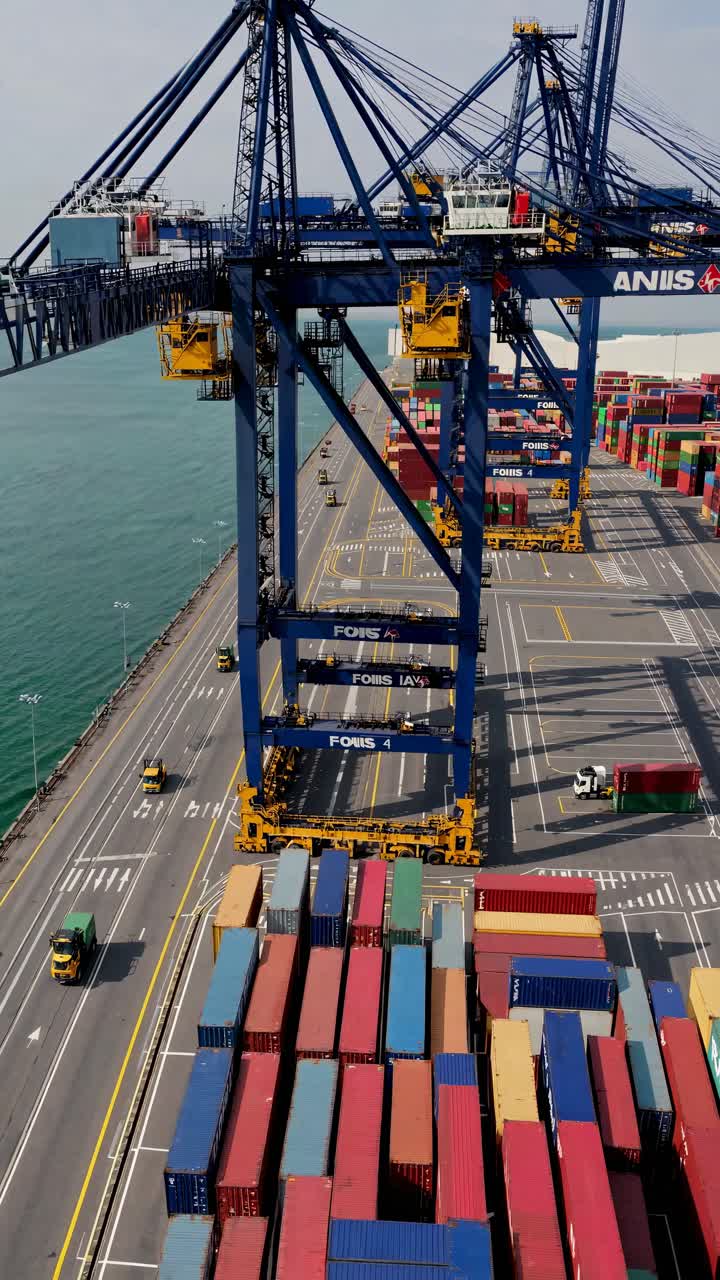 Aerial video shot of a bustling port with colorful shipping containers and towering cranes