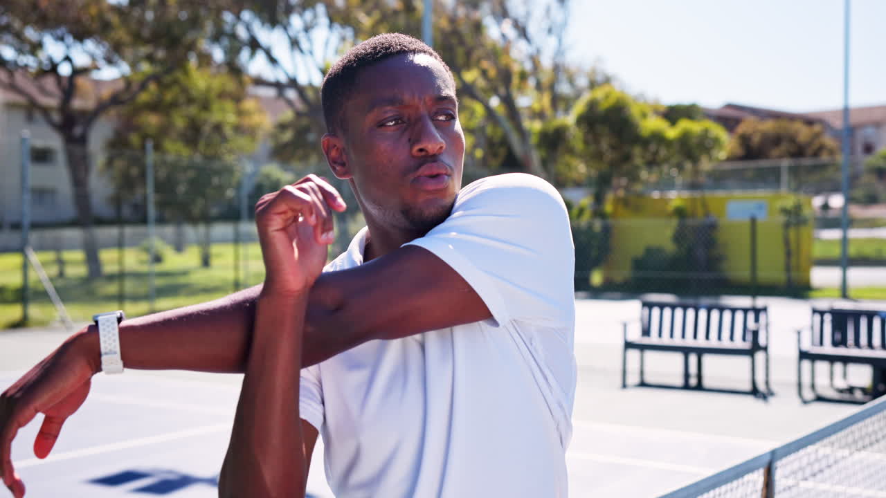 Giovane uomo di colore che allunga il braccio su un campo da tennis all'aperto