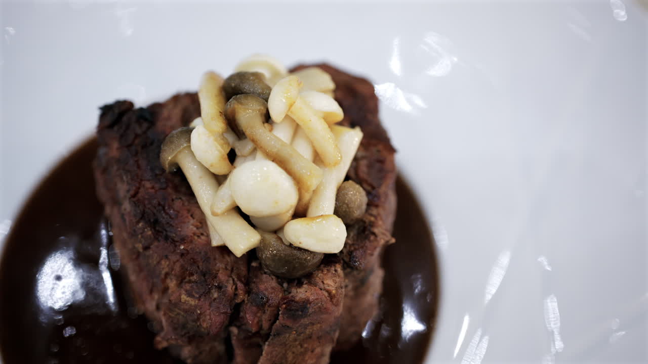 Stekt kjøtt servert med sopp og saus i et elegant restaurantmiljø.
