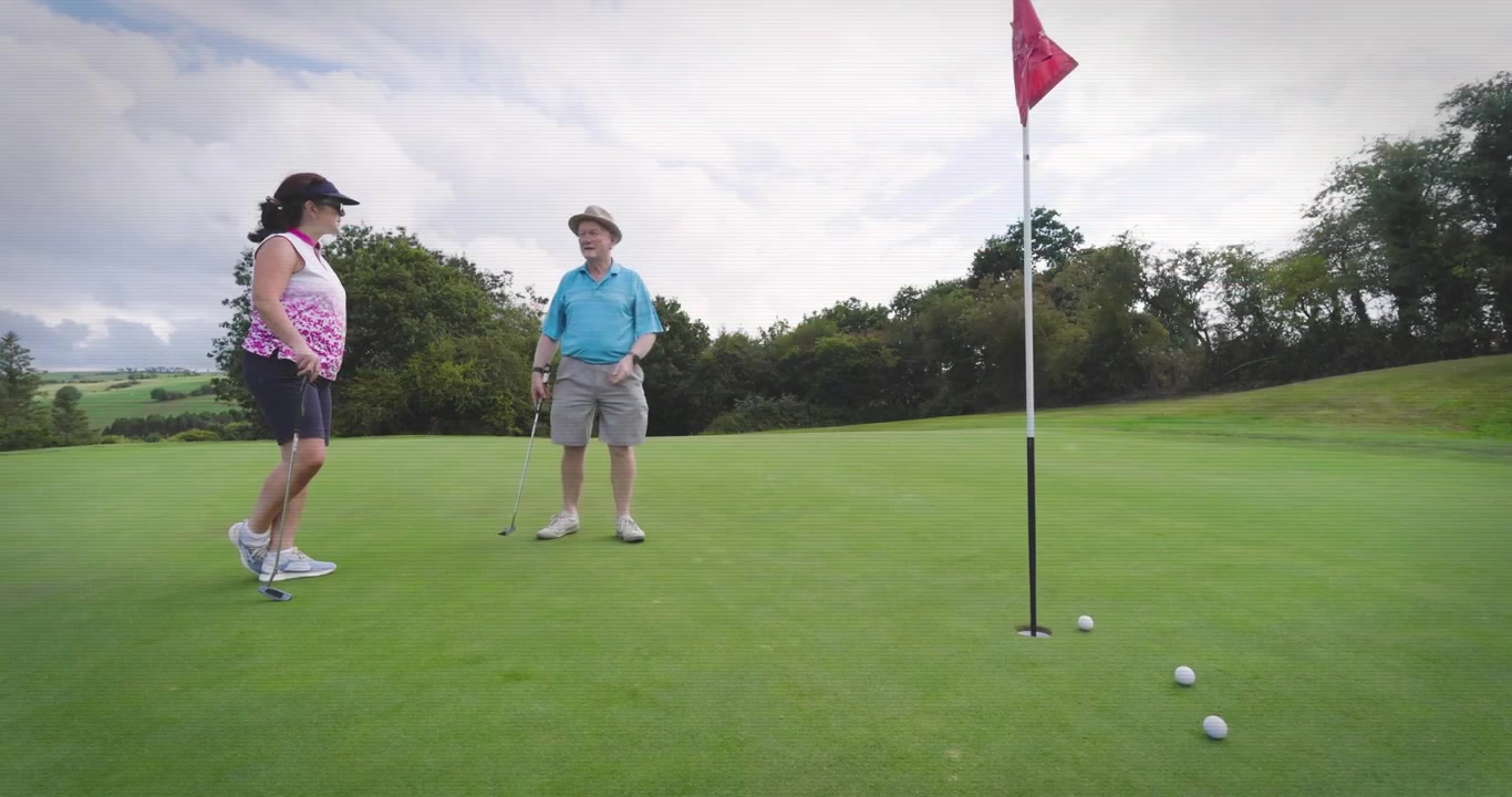 Conversazione dopo il percorso: donna che guida un uomo con il putter prima di eseguire il putt sul green da golf.