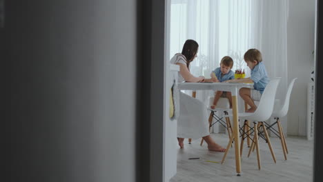 Two-children-of-boys-draw-with-his-mother-sitting-in-the-kitchen.