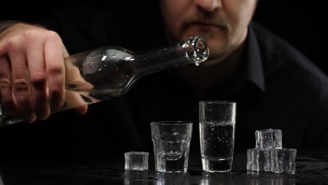 Hombre-Alcohólico-Vertiendo-Vodka-Congelado-De-Una-Botella-En-Un-Vaso-Con-Cubitos-De-Hielo-Sobre-Fondo-Negro