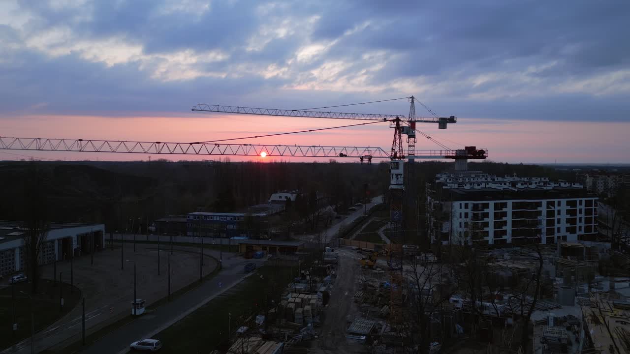 Sunset over the construction site of a prefabricated housing estate with cranes in the foreground