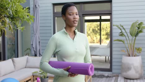 portrait of happy biracial woman holding yoga mat in garden, slow motion