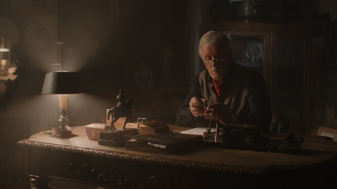 Older passionate man evaluates an old silver skull watch in his office at night
