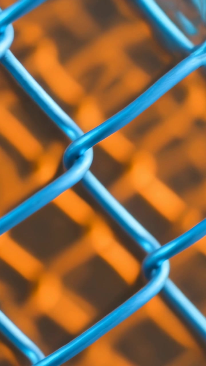 Vertikal video: Skiftende fokus får et blåt trådhegn til at bevæge sig i makro, der viser orange bokeh.