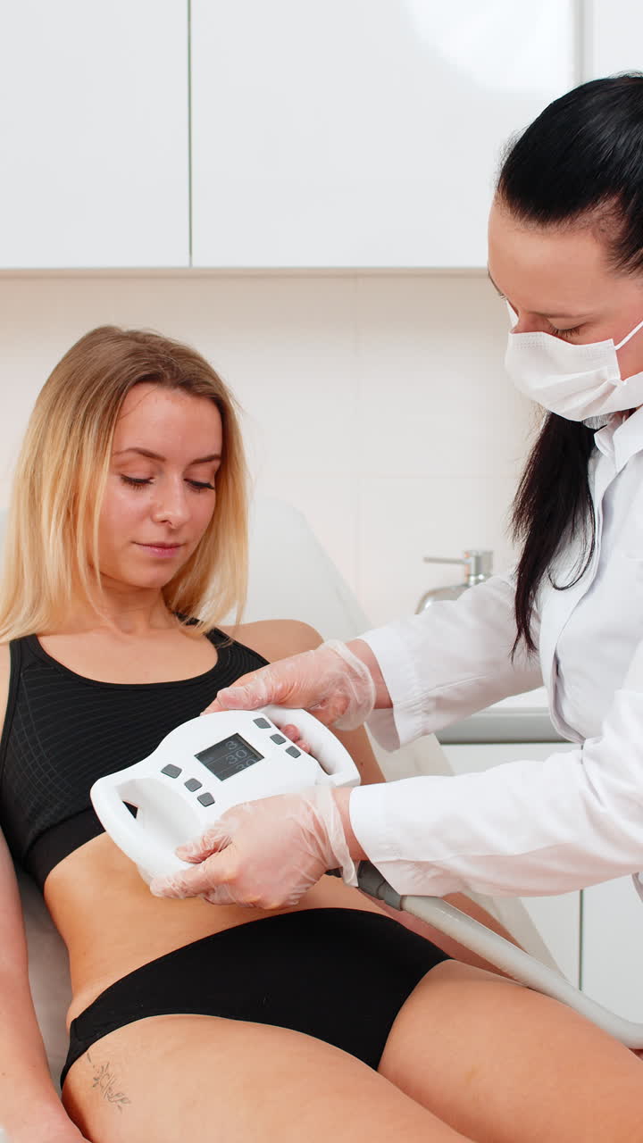 Adult woman receives abdomen vacuum massage from cosmetologist using lpg device in beauty clinic