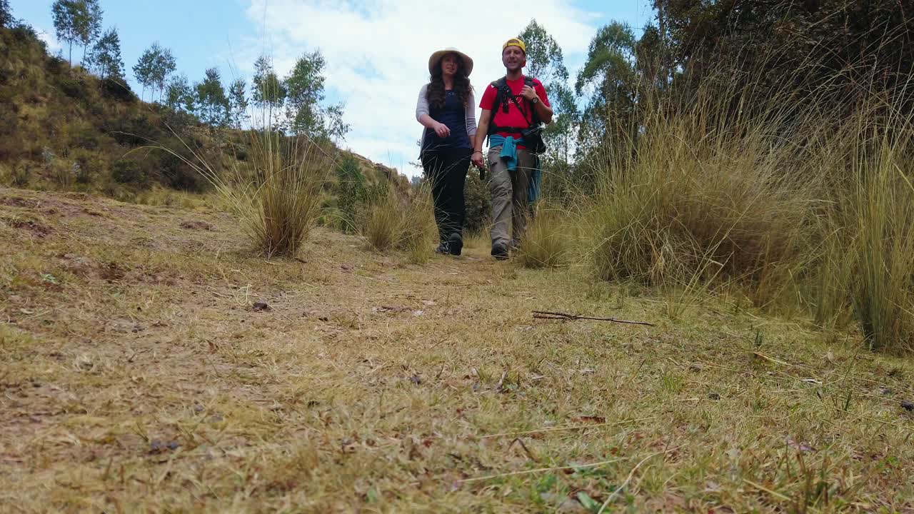 Static shot of couple holding hands, walking on old Inca Road leading from Puka Pukara to Rumiwasi. Close, couple approaching camera. Cusco, Peru
