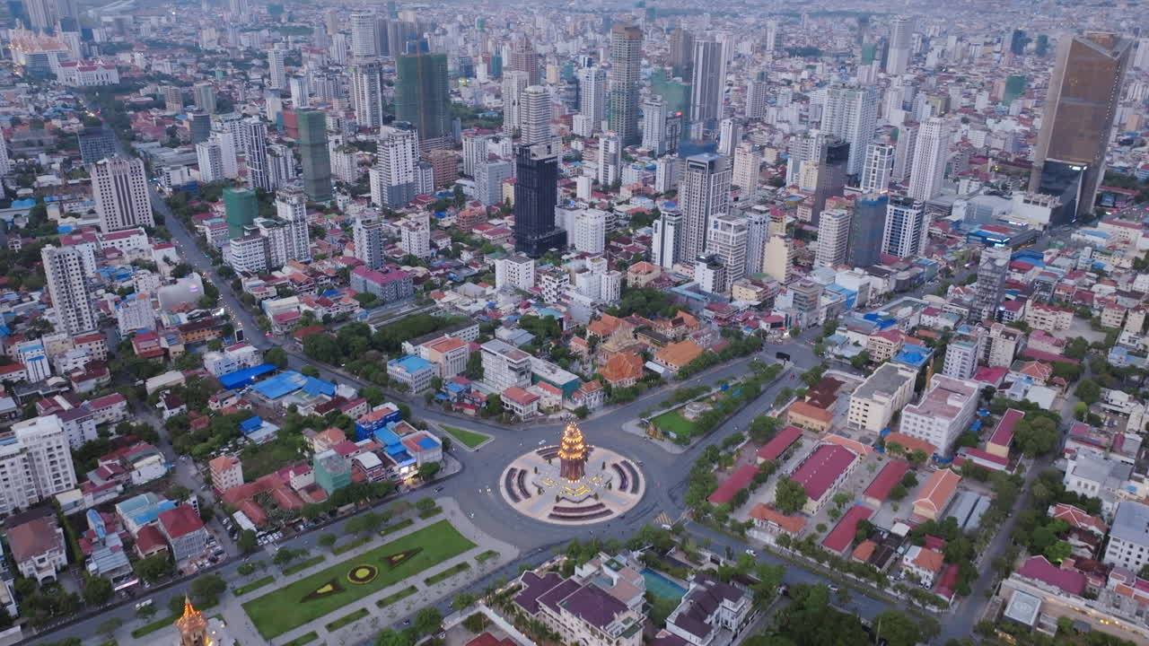 A sweeping drone view of Phnom Penh during twilight, with the Independence Monument glowing in the center and the surrounding cityscape bathed in the soft purple hues of early evening