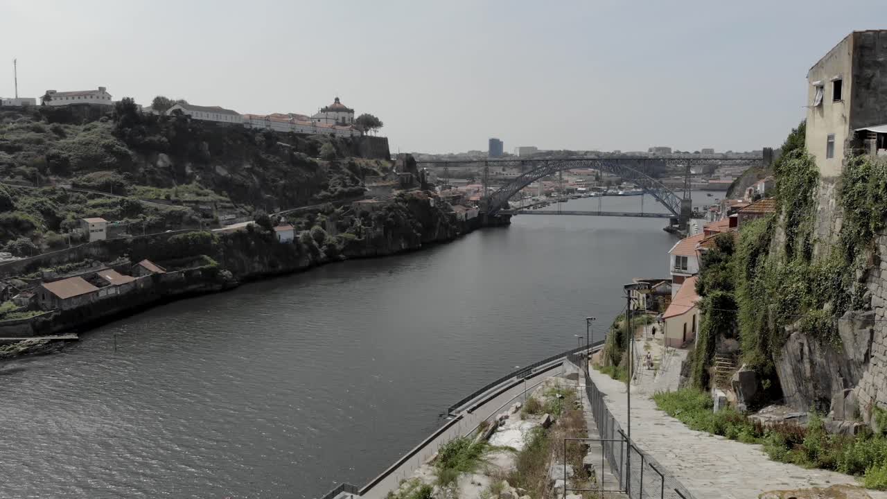 Scenic view of the Douro River in Porto, Portugal, with the Dom Luís I Bridge in the background and a woman reaching toward the camera, creating a cinematic and emotional travel moment.