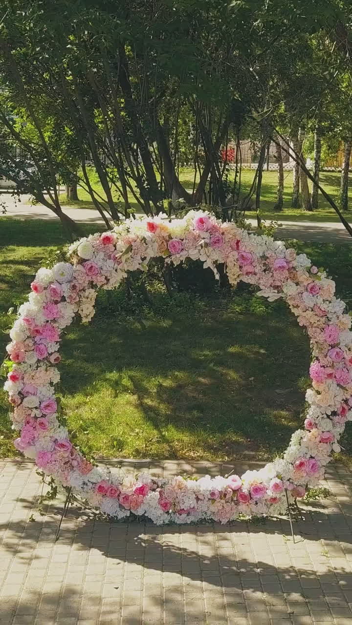 beautiful wedding venue with large round colorful flower garland and chair rows in green sunny park aerial view