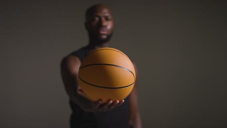 studio portrait shot of male basketball player holding ball towards camera 1