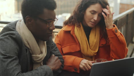 colegas multiétnicos usando computadora portátil y hablando en un café en la azotea