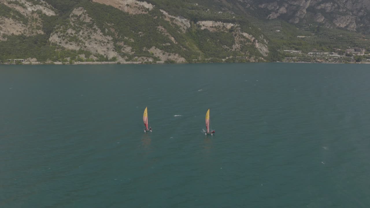Orbit droneoptagelse af sejlbåde på Gardasøen om sommeren med blå himmel og roligt vand, Italien, Norditalien, rejsedestination, Limone sul Garda, 4K 60fps slowmotion muligt, mavic 4 pro vidvinkel.