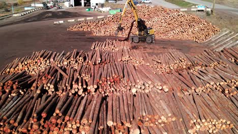 Panorámica-A-La-Derecha,-Amplia-Toma-De-Un-Dron-De-Un-Cargador-De-Troncos-En-Un-Aserradero-Que-Mueve-Troncos-Sobre-Pilas-De-Madera-En-Un-Entorno-Desértico