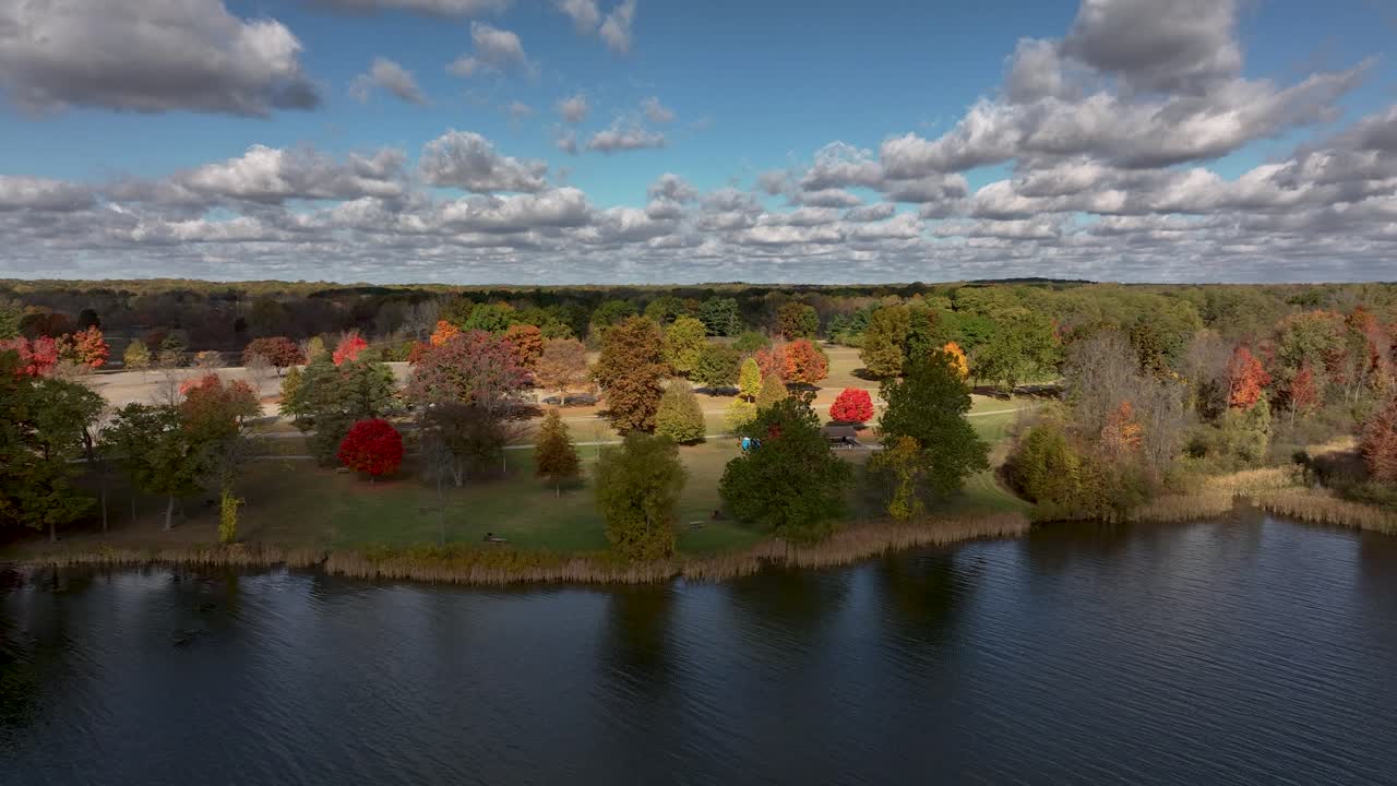 Push in drone shot from over the lake at Stony Creek Metropark in Shelby Township Michigan moving toward the shore lined with colorful trees on an autumn day