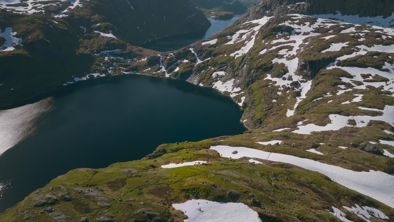 Dronekuva lennosta lumihuippuisten vuorten ja alppijärvien yli, joissa on graniittihuippuja ja kaukaisia merinäköaloja Lofootilla, Norjassa, vangiten laajan arktisen maiseman.