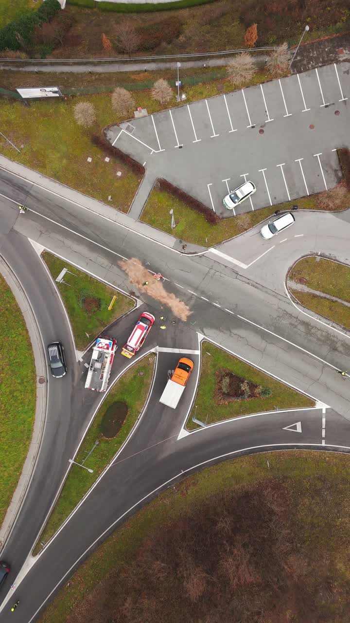 Firefighters cleaning oil spill after car accident at road intersection, top down drone vertical shot of emergency response and traffic control