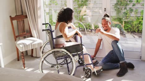 Mujer-Birracial-Feliz-En-Silla-De-Ruedas-Y-Pareja-Masculina-Sonriente-Hablando-En-Una-Sala-De-Estar-Soleada