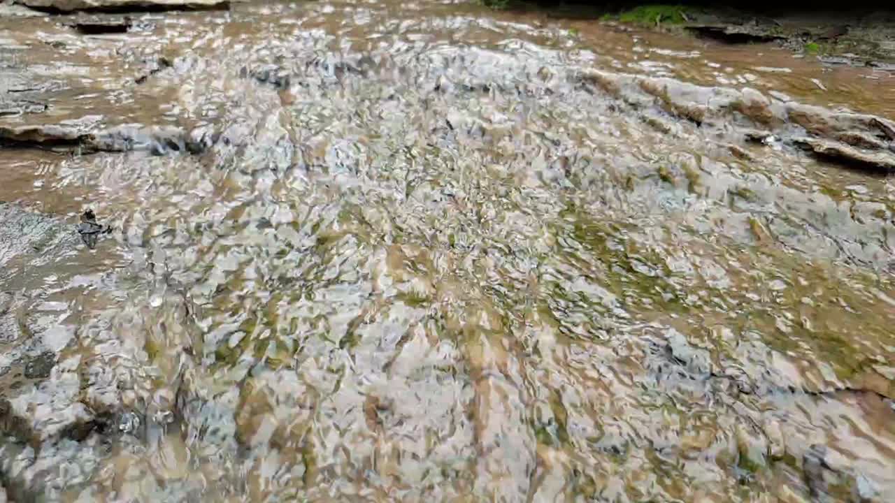 agua que fluye de un arroyo de agua de manantial de montaña que corre por enormes losas de piedra arenisca de roca con musgo verde, agua potable cristalina, meditación tranquila y pacífica en cámara lenta