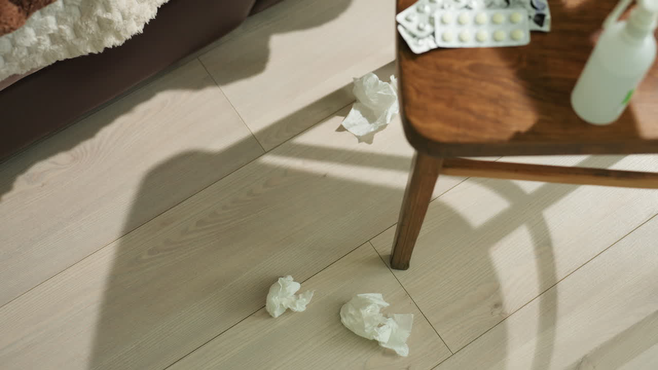 햇빛 아래 의자 근처에 놓인 티슈, 덮개와 컵이 찬장에 놓인 따뜻한 아침 풍경, 부드러운 햇살과 나무 바닥에 드리워진 곡선 그림자, 조용한 회복과 포근한 웰빙 분위기, 친밀한 인테리어