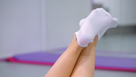 close-up of legs in white socks crossed at ankles swinging back and forth, purple yoga mat visible in background, relaxed and casual movement in indoor setting