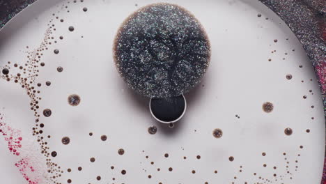 macro view of vibrating black glitter ink in a white liquid, surrounded by red and white ink droplets. the ink pulses and swirls intensely