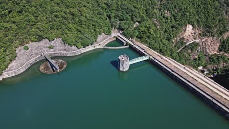A dynamic aerial shot orbiting the dam and control tower of Shing Mun Reservoir in Hong Kong